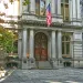 A local Historic Old City Hall building facade with large wooden doors, stone columns, American flag.