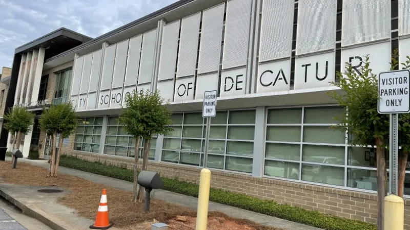 Exterior view of Decatur City School building with visitor parking signs and small trees along the sidewalk.