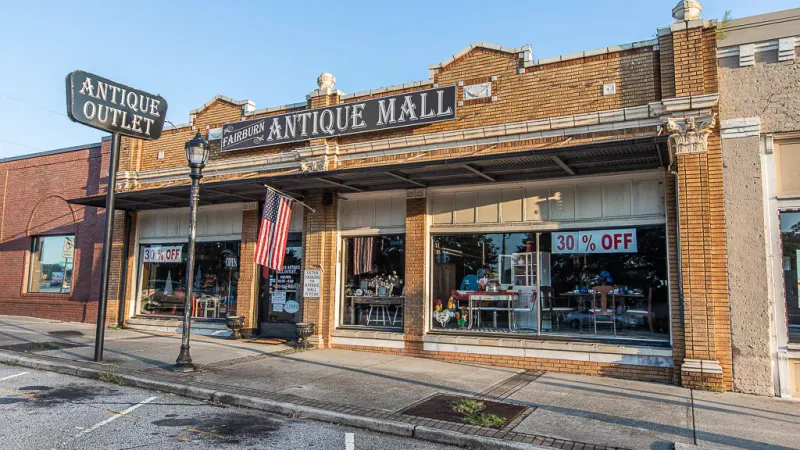 Fairburn Antique Mall storefront with American flags and 30% off sale signs on bright sunny day