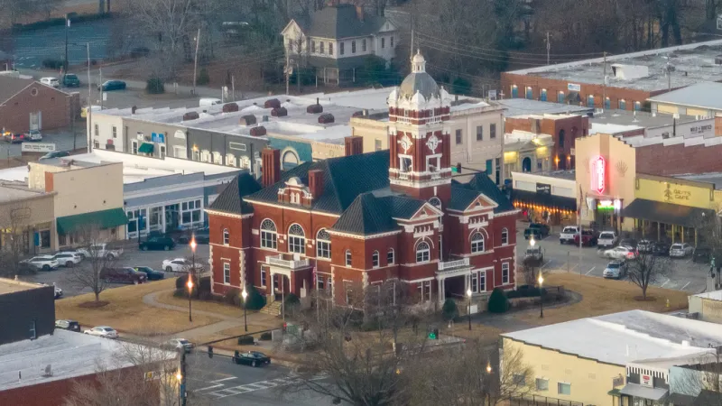 Aerial view of a historic red brick courthouse surrounded by downtown buildings and streets in a small town.