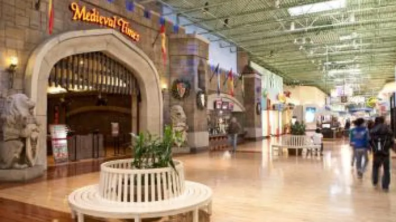 Indoor mall corridor featuring Medieval Times entrance with stone lion statues and round bench planters.