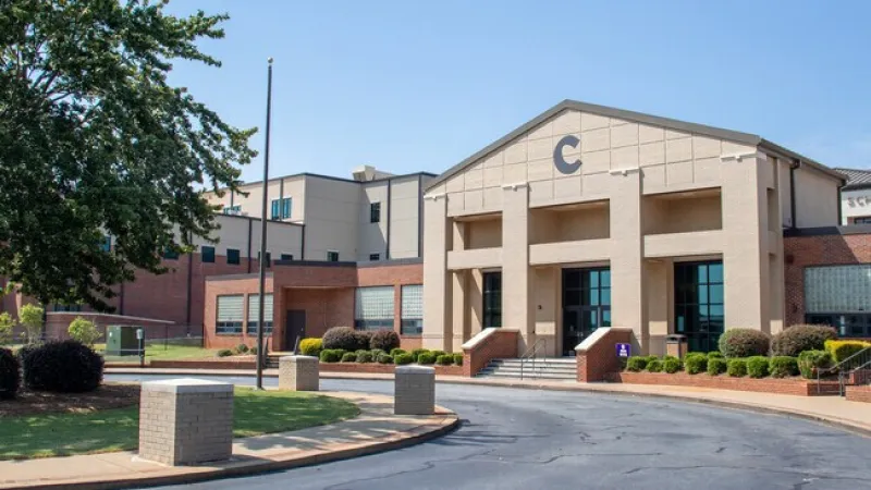 Modern school building with a central entrance labeled C, surrounded by landscaping and a curved driveway.