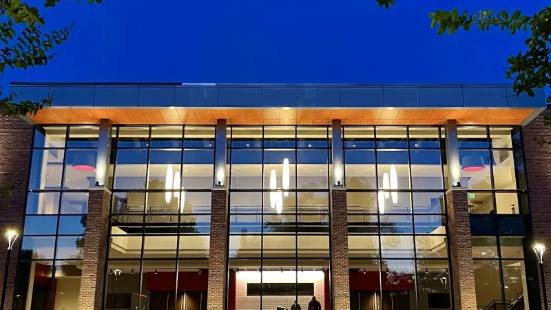 Modern glass and brick building illuminated at dusk with outdoor lighting and a deep blue sky.