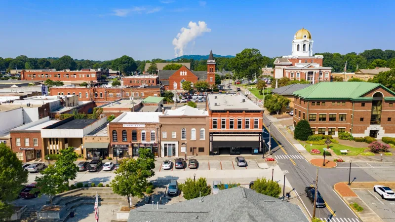 Aerial view of a small town downtown with historic buildings, a courthouse with a gold dome, and parked cars under a blue sky.