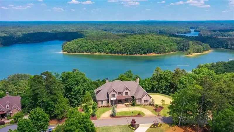 Large house surrounded by trees overlooking a winding river under a blue sky with scattered clouds.