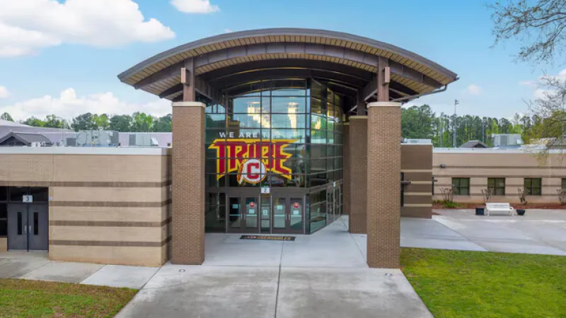 Main entrance of a modern school building with glass doors and a sign reading We Are Triple C.
