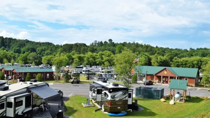 Scenic RV park with motorhomes, cabins, and green trees under a partly cloudy sky.