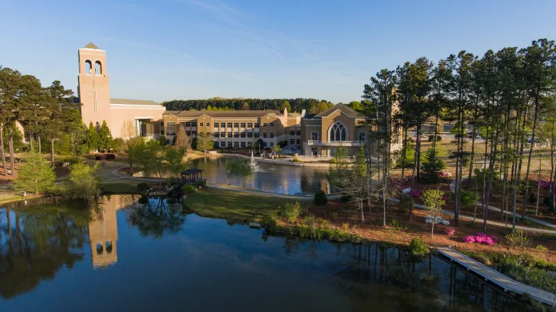 Modern university campus with a bell tower, large pond, green trees, and clear blue sky on a sunny day
