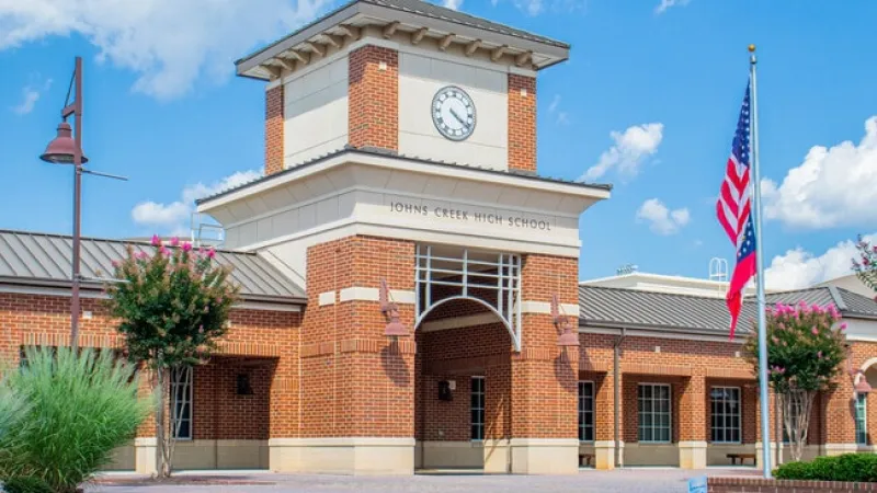 Johns Creek High School brick building with clock tower and American flag against blue sky