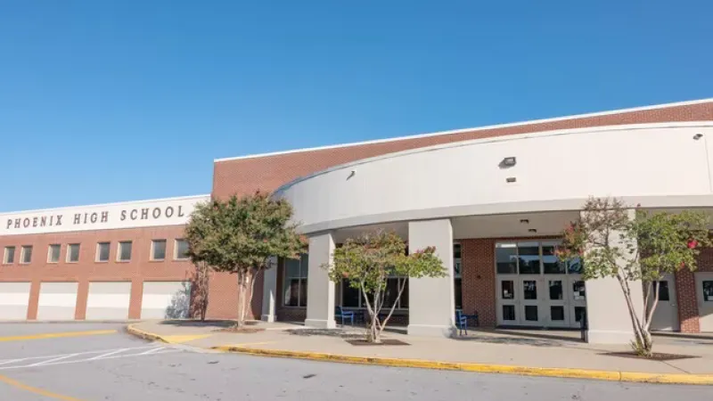 Entrance of Phoenix High School with brick facade, trees, and a clear blue sky.