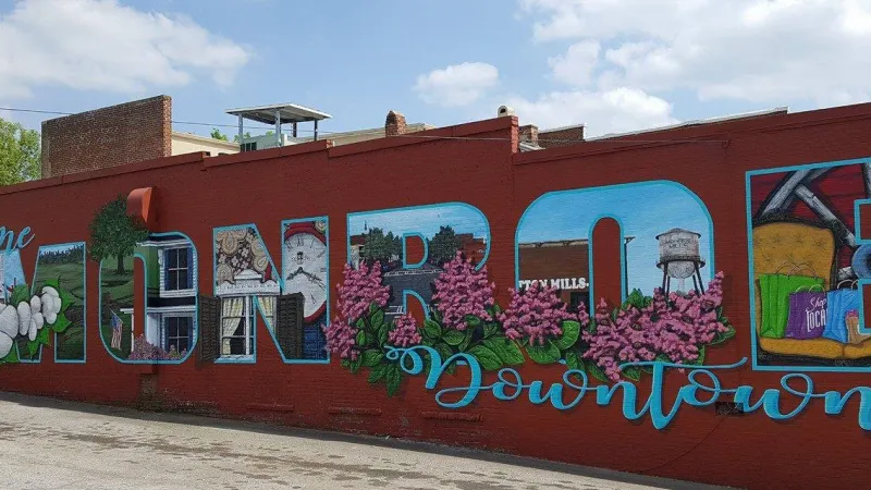 Colorful mural on red brick wall welcoming visitors to Monroe Downtown with floral and local imagery.