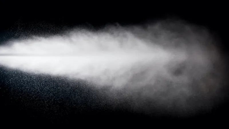 White mist or spray dispersing in the air against a black background, showing fine water droplets and vapor.