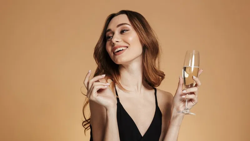 Smiling woman in black dress holding a glass of champagne against brown background