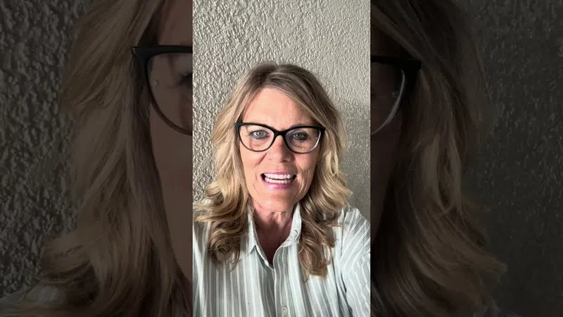 Smiling woman with glasses and wavy blonde hair wearing a striped shirt against textured wall background