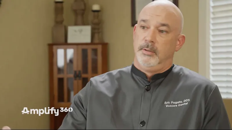 Bald man in dental coat with Eric Fugate DDS Vonore Dental logo in calm office setting speaking.