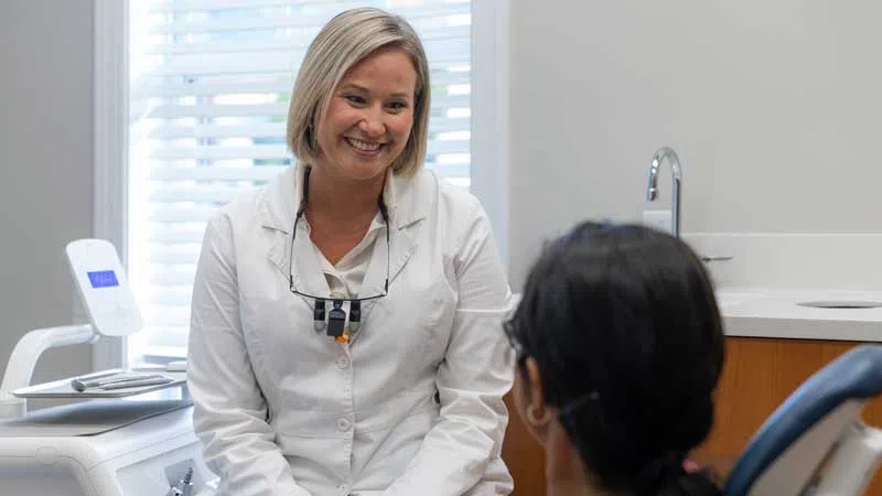 Female dentist smiling and talking with patient in a bright dental office with equipment in background