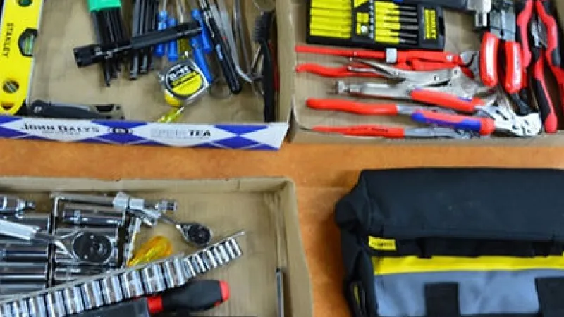 Various hand tools including pliers, screwdrivers, wrenches, and a tool bag neatly arranged on a surface.
