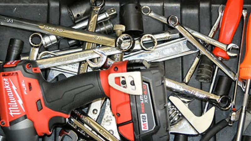 Red and black Milwaukee cordless drill surrounded by wrenches and orange-handled screwdrivers in a toolbox.