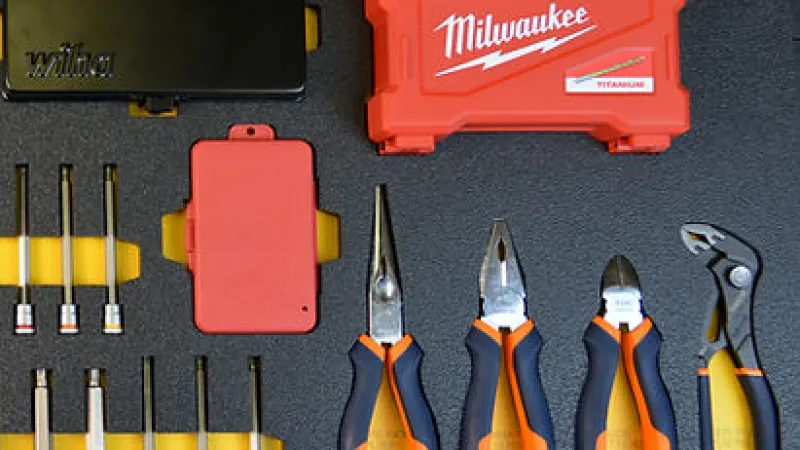 Set of Milwaukee hand tools including pliers, sockets, and red storage cases neatly arranged on a black surface