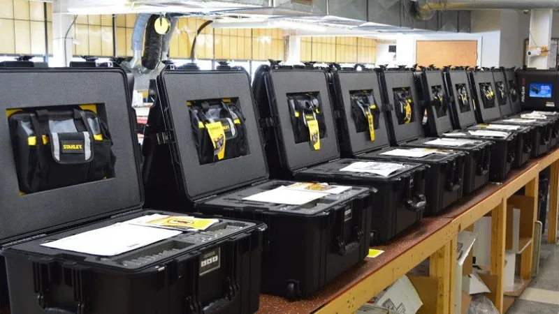 Row of open black hard cases with tools and manuals inside on a wooden workbench in workshop.