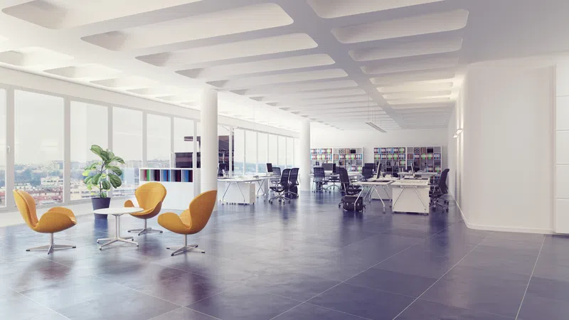 Bright modern open office space with large windows, ergonomic chairs, desks, and yellow lounge seating area.