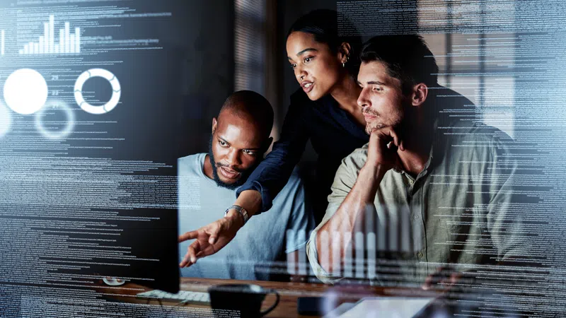 Three diverse professionals analyzing data charts and code on a transparent digital screen in a modern office.