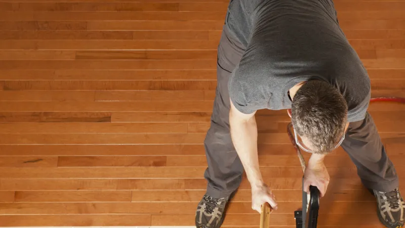 Man installing hardwood flooring using a rubber mallet and flooring nailer from above view