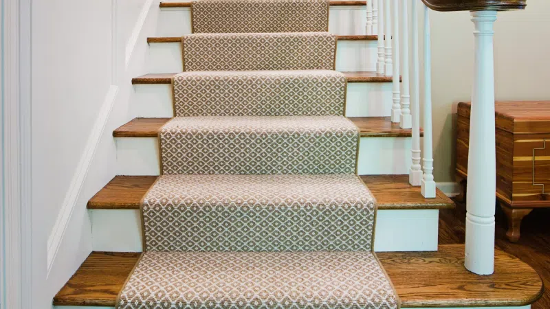 Wooden staircase with beige patterned carpet runner in a bright white walled interior.