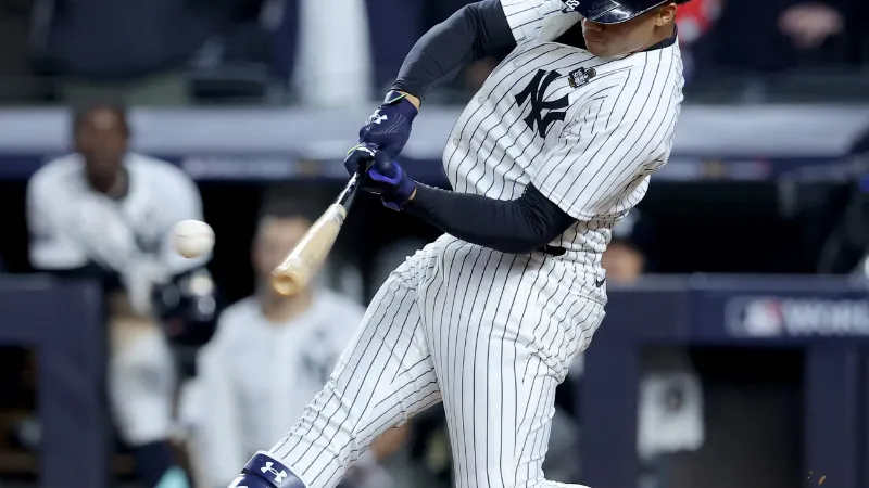 New York Yankees player hits a baseball during a game, wearing pinstripe uniform and helmet in action.