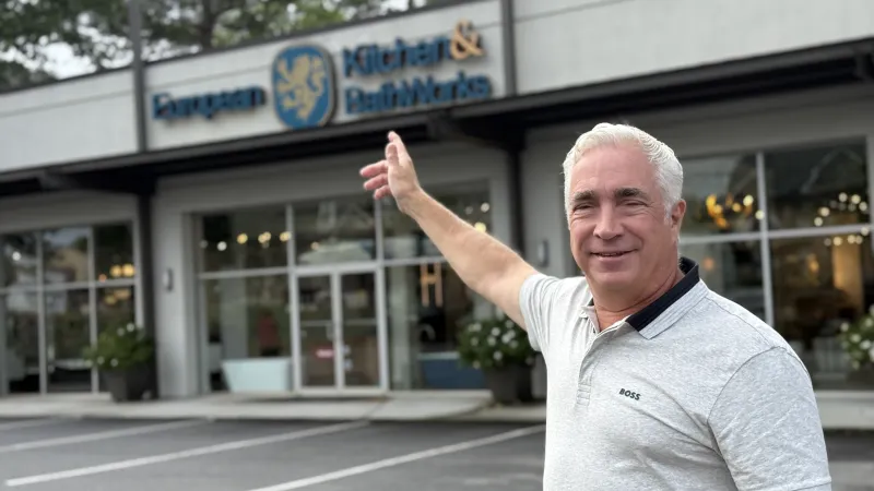 Smiling man in light gray polo outside European Kitchen & Bath Works showroom pointing at the building.