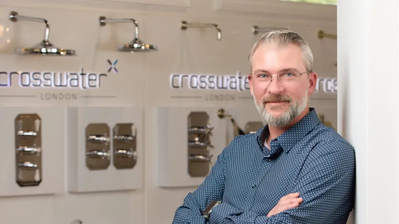 Confident man with glasses poses with arms crossed in showroom featuring Crosswater London faucets and fixtures.