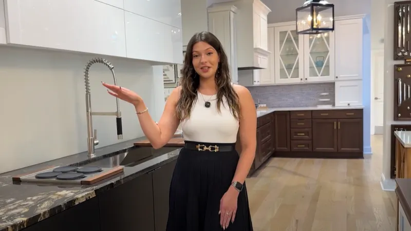 Woman presenting a modern kitchen with black and white cabinetry and a high-arc pull-down faucet in a showroom.