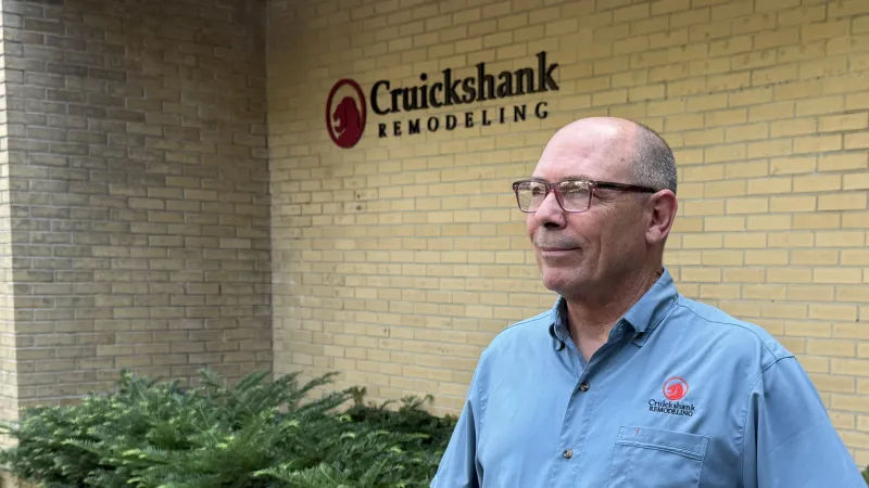 Man in blue Cruickshank Remodeling shirt standing confidently outside a yellow brick building with company sign