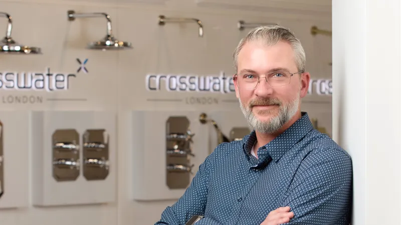 Smiling man with glasses and beard standing confidently in front of Crosswater London faucet displays