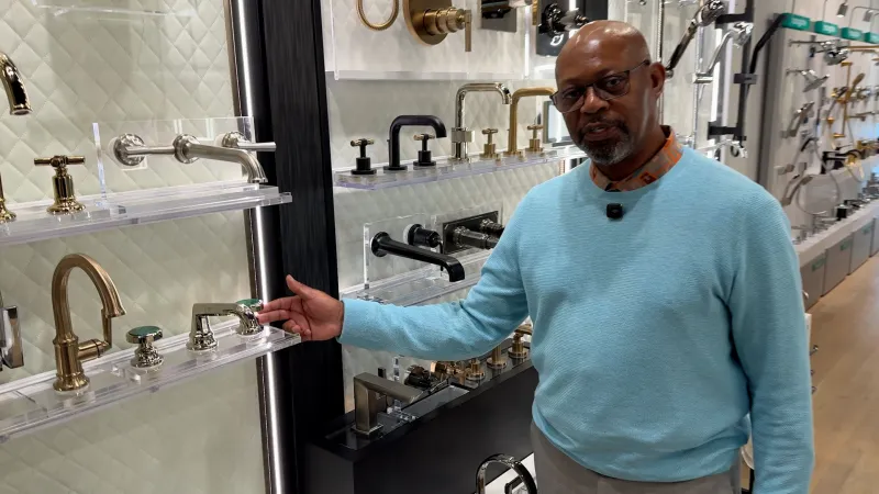 Man in blue sweater showcases various modern faucet designs in a sleek, well-lit showroom display.