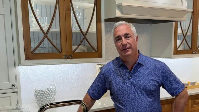 Man in blue shirt standing in modern kitchen with wooden cabinets and white countertop