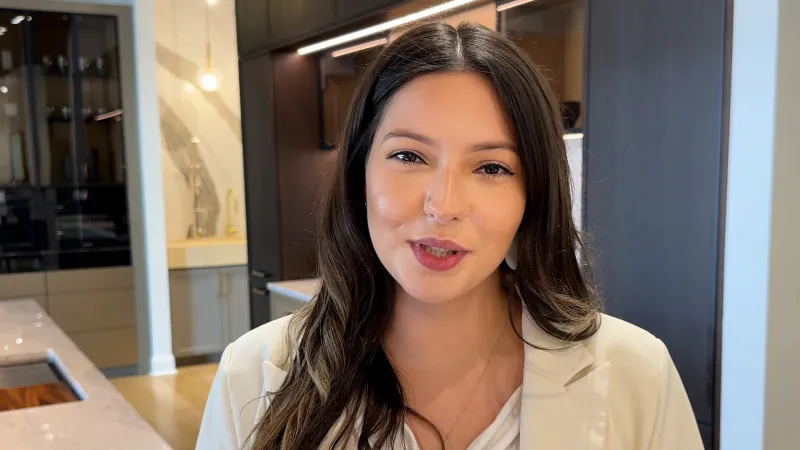 Young woman with long dark hair smiling in a modern kitchen with beige and dark wood accents.