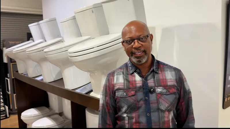 Man standing beside a row of white toilets displayed on shelves in a showroom or store.