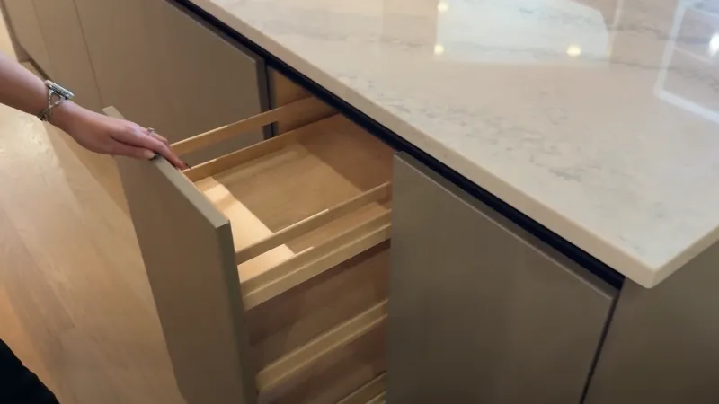Hand opening a wooden drawer in a modern kitchen island with marble countertop and hardwood floor.