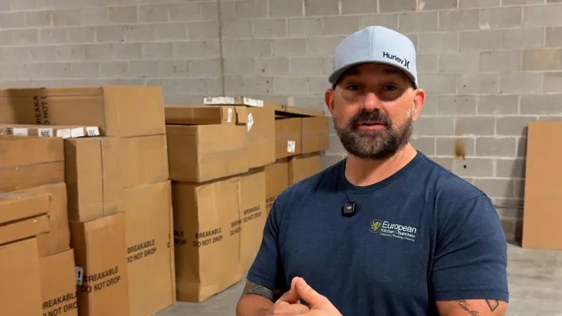 Man wearing Hurley cap and European Shipping Solutions shirt stands in warehouse with stacked cardboard boxes.