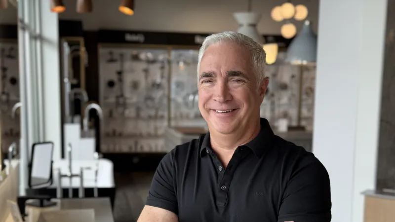 Smiling man with crossed arms stands in a modern showroom with faucets and lighting fixtures in background
