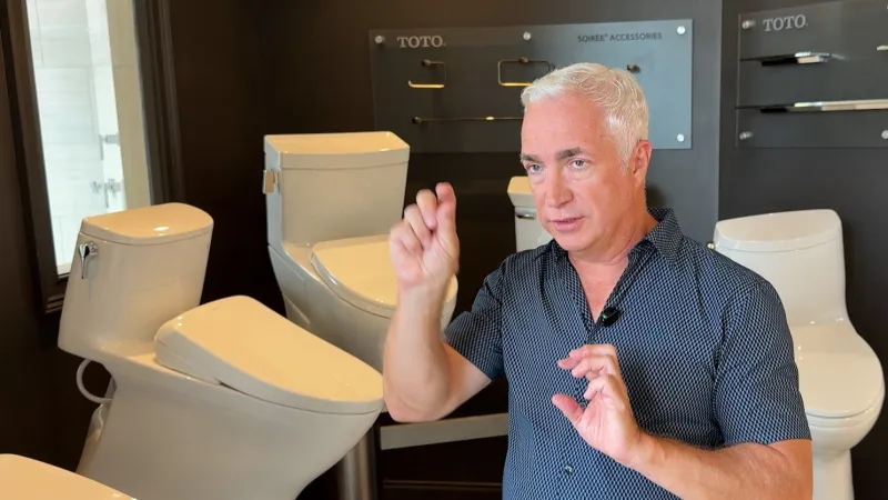 Man explaining features of modern toilets displayed in a showroom with brand Toto visible in the background