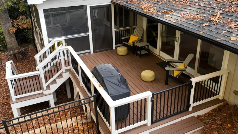 Spacious outdoor deck with seating, grill, and colorful cushions surrounded by autumn leaves.