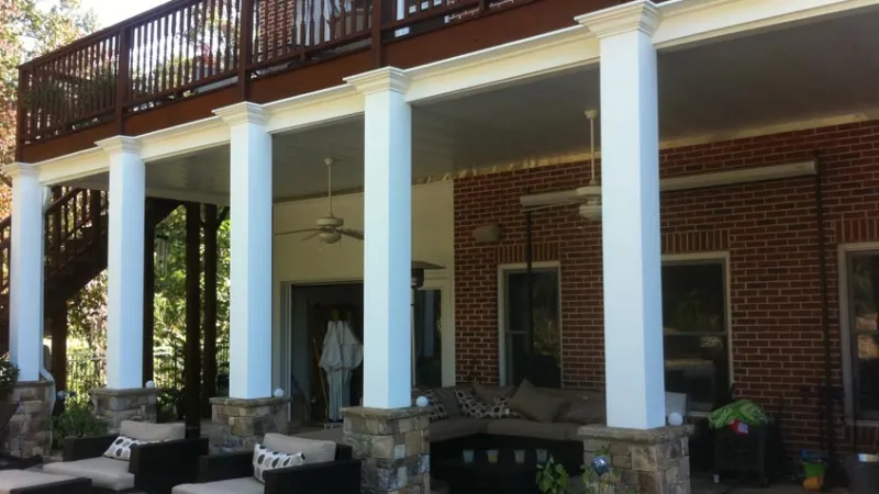Covered patio with stone pillars, white columns, ceiling fans, and outdoor furniture under a wooden deck.