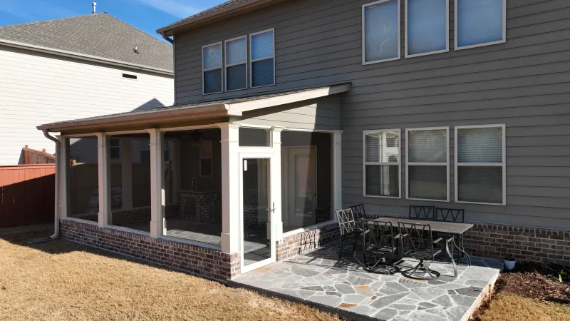 Backyard patio with screened porch and stone tile seating area attached to beige two-story house