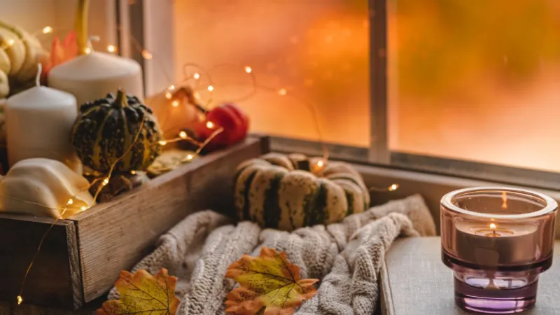 pumpkin and candle and blanket sitting beside window