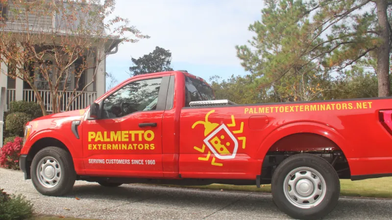 Red Palmetto Exterminators truck parked in front of a house with pest control logo and contact website.