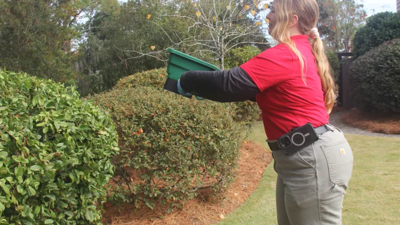 a woman holding a green bin applying pest control