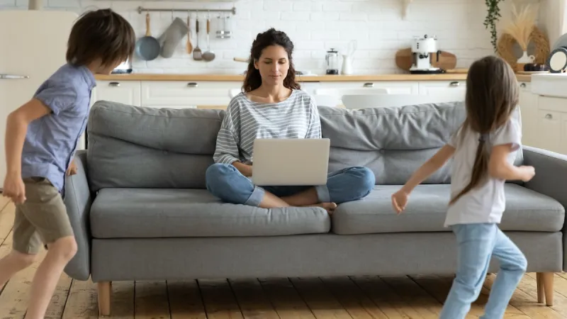 a woman and two children sitting on a couch looking at a laptop