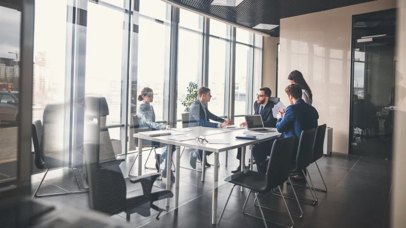 Business team having a meeting around a table in a modern office with large windows and city view.